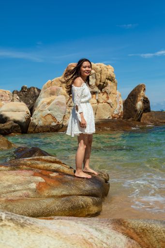 A vertical shot of a pretty Asian girl standing on rocks near the blue ocean in Vietnam