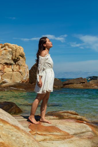A vertical shot of a pretty Asian standing on rocks near the ocean in Vietnam