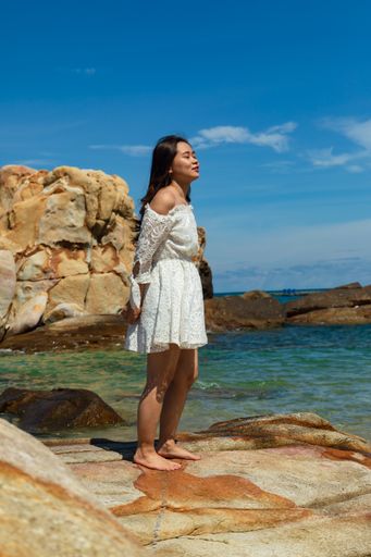 A vertical shot of a pretty Asian girl standing on rocks near the ocean in Vietnam