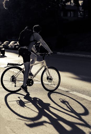 A vertical shot of a cyclist waiting to cross the road with his reflection on the ground