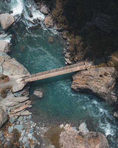 A vertical aerial shot of a wooden bridge over a lake connecting two hills