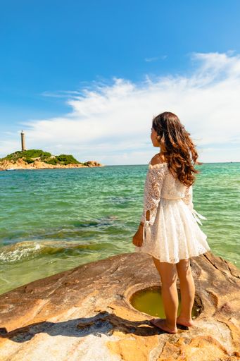 A vertical shot of a young lady on the seashore on a cloudy day