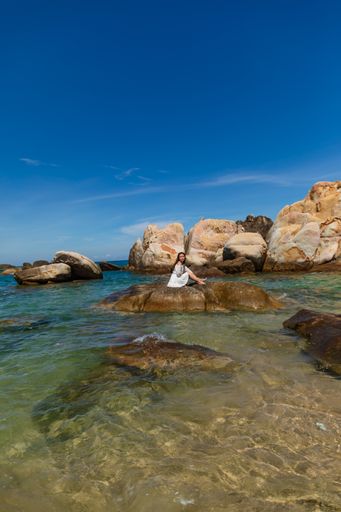 A vertical shot of a beautiful young lady sitting on a rock on the seaside