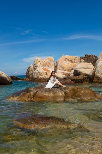 A vertical shot of a beautiful young lady sitting on a rock on the seaside