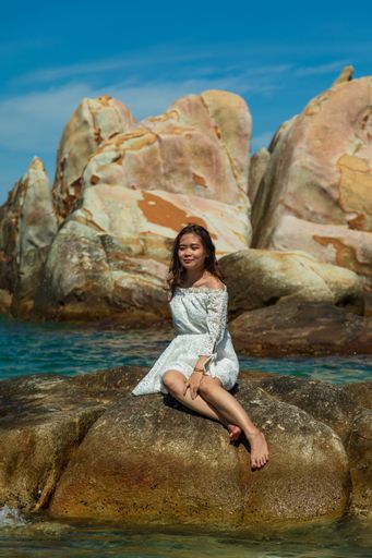 A vertical shot of a beautiful young lady sitting on a rock on the seaside