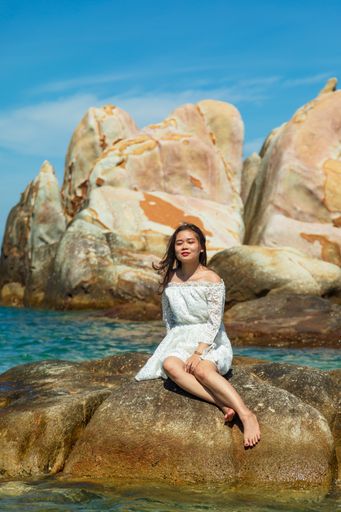 A vertical shot of a beautiful young lady sitting on a rock on the seaside