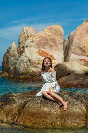 A vertical shot of a beautiful young lady sitting on a rock on the seaside
