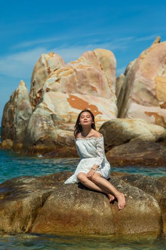 A vertical shot of a beautiful young lady sitting on a rock on the seaside