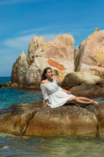 A vertical shot of a beautiful young lady sitting on a rock on the seaside