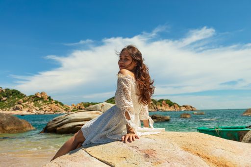 A beautiful shot of an attractive Asian woman in a summer dress sitting on a beach stone