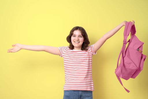 Portrait of a happy schoolgirl smiling with a pink backpack, looking at camera, on yellow background