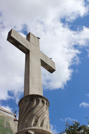 A vertical shot of an outdoor stone cross under a blue cloudy sky