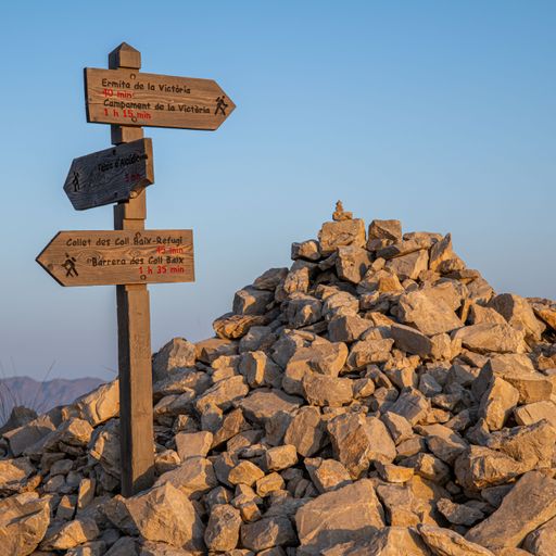 A vertical closeup of a wooden direction signpost on the pile of stones and cairn on Mallorca
