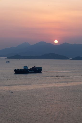 A vertical shot of a sunset over sea with a boat in it at Lamma Island, Hong Kong