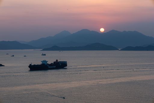 A beautiful pink sunset sky over the sea with a large cargo ship and silhouettes of mountains, Lamma Channel, Hong Kong