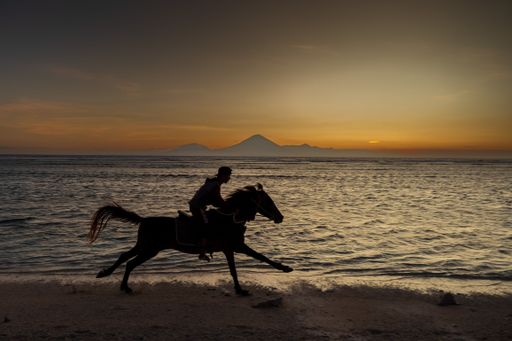 A scenic view of a person riding a horse in a beautiful sandy beach during a breathtaking sunset