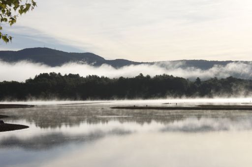 A scenic view of a lake against green hills covered with fog in New Hampshire