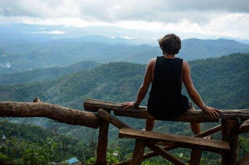 A man sitting on the wooden fence and enjoying the mesmerizing landscape of green hills, shot from back