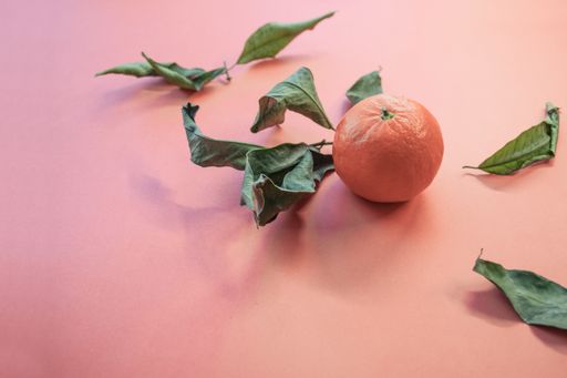 A closeup shot of a fresh orange tangerine with its green leaves spread on a light pink background