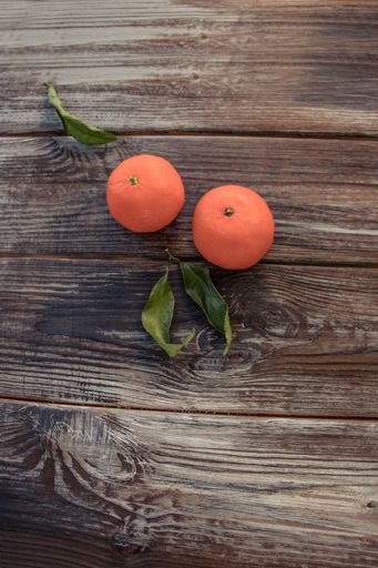 A vertical still life image of two fresh orange tangerines and green leaves on a wooden surface