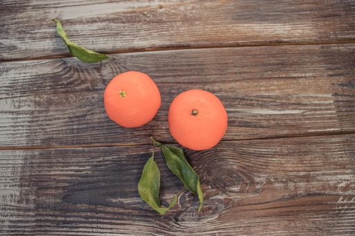 A still life image of two fresh orange tangerines and green leaves on a wooden surface