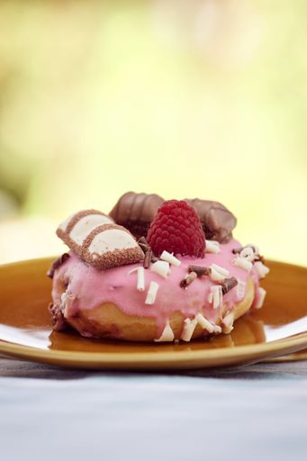 A tasty donut topped with fresh berries and chocolates on a saucer, vertical shot