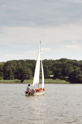 Two silhouettes of people on a wooden boat, peacefully enjoying a scenic lake surrounded by green trees