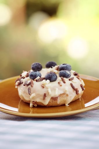 A tasty donut topped with cream and blackberries on a saucer, vertical shot