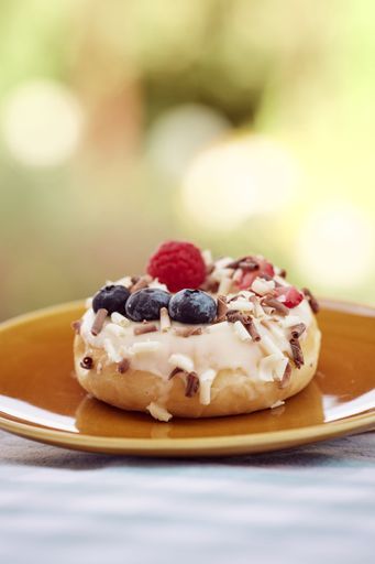A tasty donut topped with fresh berries on a saucer, vertical shot