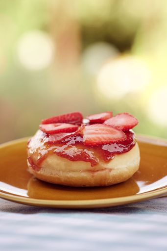 A tasty donut topped with fresh sliced strawberries on a saucer, vertical shot