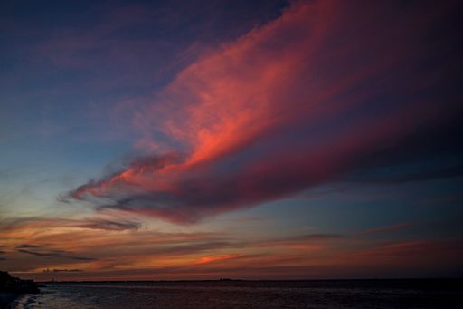 A beautiful view of the calm sea under an amazing pink cloud with the colorful sky in the background