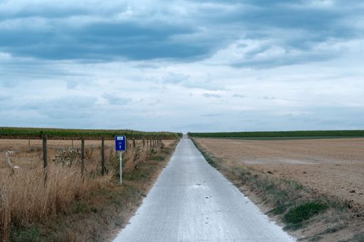 A straight road and feild in the countryside under a cloudy sky