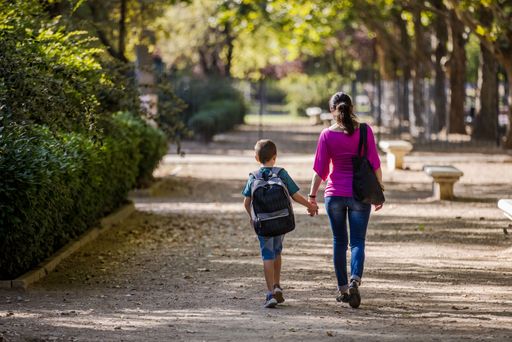 The view from behind of the mother and son walking to the school through the park