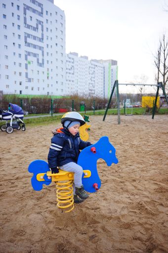 Young boy with safety helmet sitting in a spring swing at a playground.