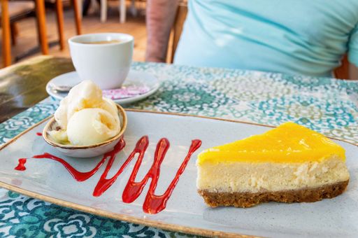 A close up shot of a vanilla cheesecake dessert with ice cream ball and coffee cup.