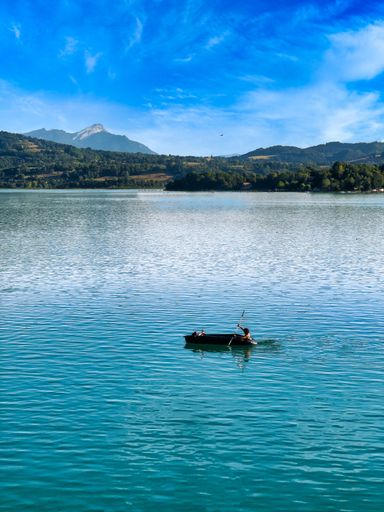 A vertical shot of a person on a boat sailing in a lake against green hills