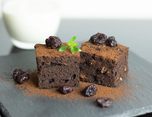 A closeup of two slices of chocolate brownies with cherries and cocoa powder