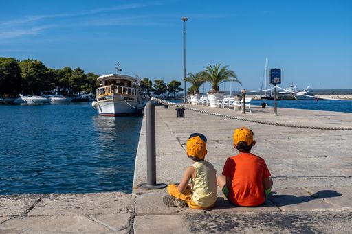 Two boys sitting on a harbor watching a boat in Brijuni, Croatia