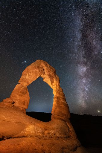 A vertical shot of a stone arch formation under a milky way galaxy sky