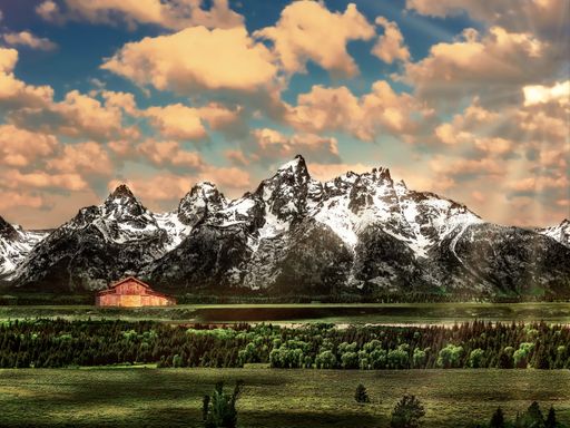 A beautiful shot of the Grand Teton National Park in Wyoming with snowy mountains and a wooden barn in the distance