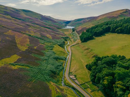 A beautiful shot of the Glencorse Reservoir next to a road and surrounded by green mountains