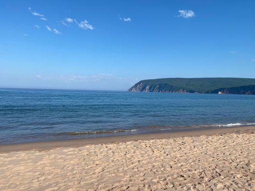 A scenic view of a calm isolated beach with sand dunes and a hill in the background