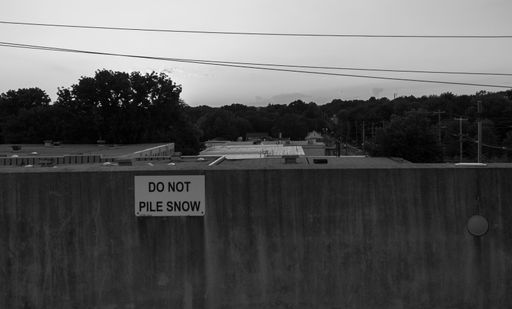 A black and white shot of a "Do not pile snow here" street sign on a wall with nature in the background