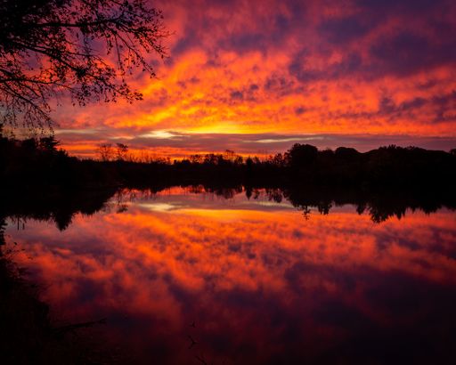 Epic scarlet sunset sky above the lake and forest in autumn. Dramatic cloudscape. Symmetry reflections on the water, natural mirror.