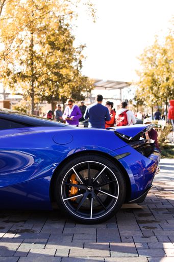 A vertical closeup shot of a blue sports car with blurred people in the background at daytime