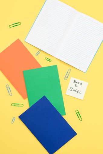 top view of colorful back to school note with notebook and clip on yellow background