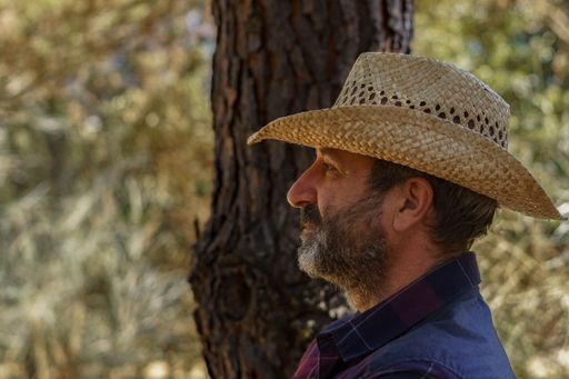 close-up of a man with beard and hat in profile in the forest with a tree in the background