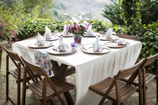 A table full of plates and a flower vase on a beautiful balcony with an amazing view in the background