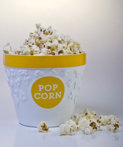 A vertical shot of a basket full of popcorn and some popcorn on around it on a white background