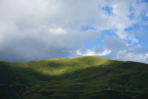 A scenic shot of white fluffy clouds in the sky with green-covered hills under them